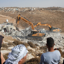 People watch two bulldozers destroy a house