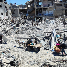 Young men push a bicycle and ride a donkey-drawn cart carrying their possessions along a bombed-out road