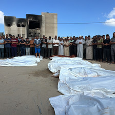 People pray over a row of shrouded corpses