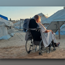 With his back to the camera, a man sits in his wheelchair amid tents in the sand