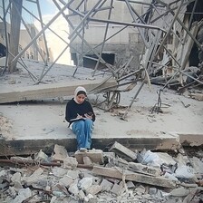 A woman sits studying in rubble