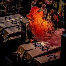 A person holds a flare emitting fiery-looking orange smoke while standing next to coffins draped in Israeli flags