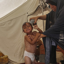 A woman bathes her child with a cup of water