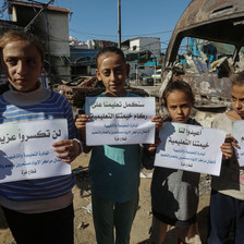 Children hold protest signs amid Israeli destruction in Deir al-Balah