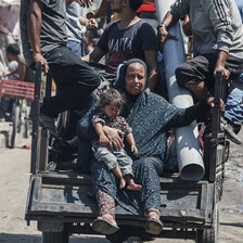 A woman and a child sit on the back of a cart pulled by a donkey