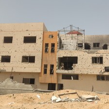 A daytime view of a building riddled with bullet holes and damage from explosives.