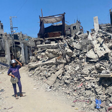 A boy wearing a pot as a helmet walks through rubble