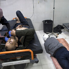 Two patients lie on the floor next to one occupied hospital bed