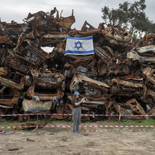 A woman takes a selfie in front of a stack of crushed cars and an Israeli flag