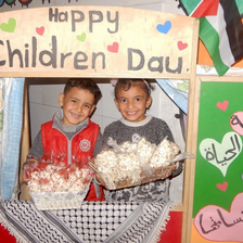 A boy and girl hold baskets while standing behind frame decorated with Palestinian symbols