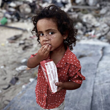 A young girl holds a small bag in one hand while raising another hand to her mouth