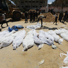 Corpses wrapped in white shrouds are spread across sand ground