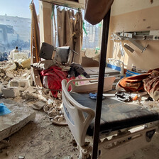 In the daytime, a destroyed hospital room is seen with one of its walls totally missing and with a view of more destruction outside