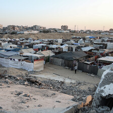 Rows of makeshift tents beside a sand dunes and buildings in southern Gaza 