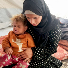 A woman holds her small child on her lap in a tent. 