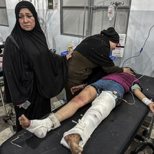 Woman with sad expression stands next to injured girl on stretcher in hospital