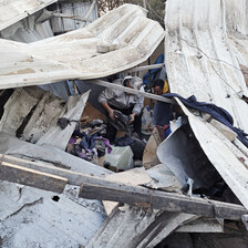 Men sort through personal belongings in a destroyed makeshift shelter