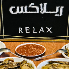 A sign for Relax Cafe in Arabic and English sits on a table of various dishes of food
