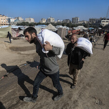 two men carry large bags of flour