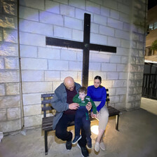 A couple and a toddler sit under a large cross