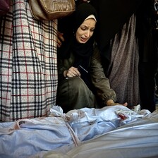 A kneeling woman cries while reaching towards a shrouded body on the ground