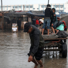 A bare-footed man wearing a baseball cap pulls a loaded cart carrying multiple children