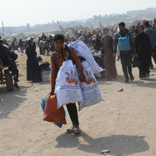 A child with heavy bags amid a crowd of people on foot