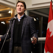 Canadian Prime Minister Justin Trudeau stands behind a microphone and in front of a Canadian flag 