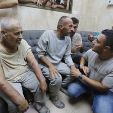 Five Palestinian men seated or squatting with more people in background