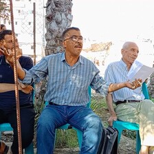 A man speaks and gestures with hands while sitting on a chair on a sunny day