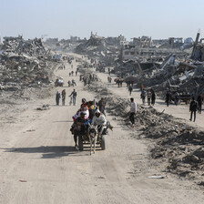 A cart traverses a dust road in a bleak landscape of destroyed buildings