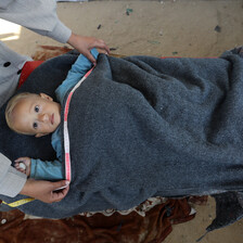 An aerial view of a baby under a blanket, with two hands measuring the blanket.