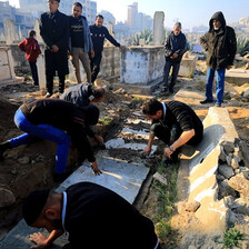 Men stand and sit next to white casket lowered into the ground