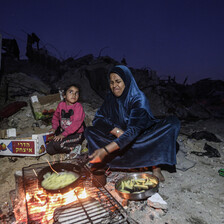 A mother and child prepare food over an open fire