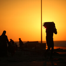 A man in silhouette against a setting sun carries a gas canister