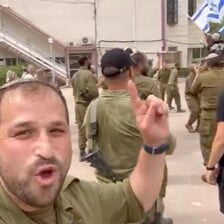 A man in an Israeli army uniform gestures at an Israeli flag