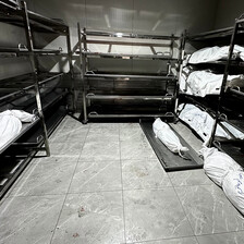 A room with metallic bunk beds, each shelf with a corpse wrapped in white