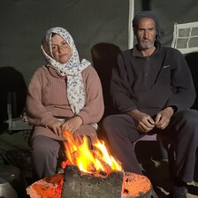 A woman and a man sit behind a fire