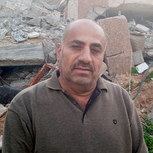 A close-up of man in a collared shirt in front of piles of rubble