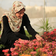 A smiling young woman kneels over a bed of flowers