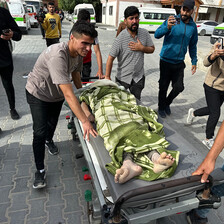 A few men wheel a trolley on which the body of a boy killed by Israel has been laid