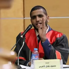 A man wearing graduation regalia speaks into the microphone. 