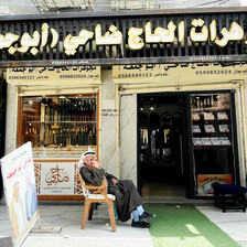 An older man sits in a plastic chair in front of a jewelry shop