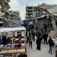 People walk past a small stall amid destroyed buildings 