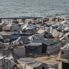 Dozens of tents are set up on the sand, with a view of the ocean in the background.
