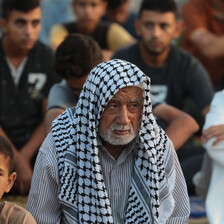 A close-up of an elderly man with a black-and-white checkered kuffiyeh draped over his head. 