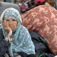 An older woman hold her head in her right hand while sitting in front of personal belongings