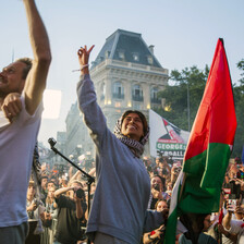 Woman wearing gray sweatshirt smiles while looking up and holding fist up in the air in front of massive crowd