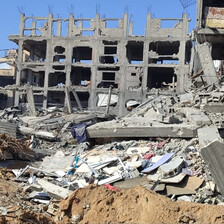 Landscape view of skeleton of badly damaged mid-rise building with rubble strewn in front