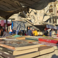 A  pile on the books in the foreground and man apparently reading behind